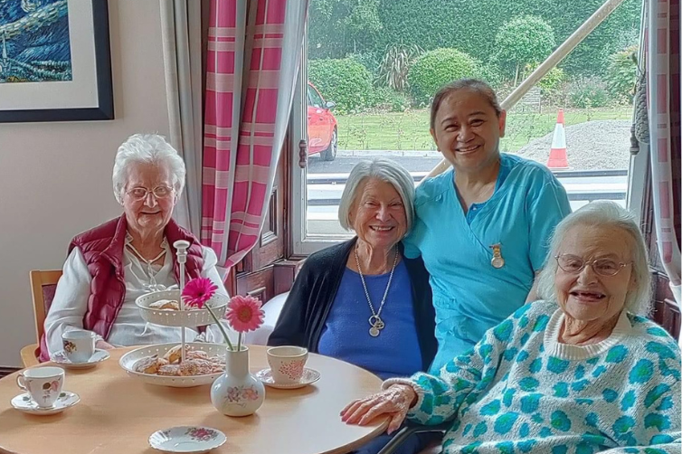 Photo of three resident lafies and a healthcare worker smiling while drinking tea in Greystones Nursing Home