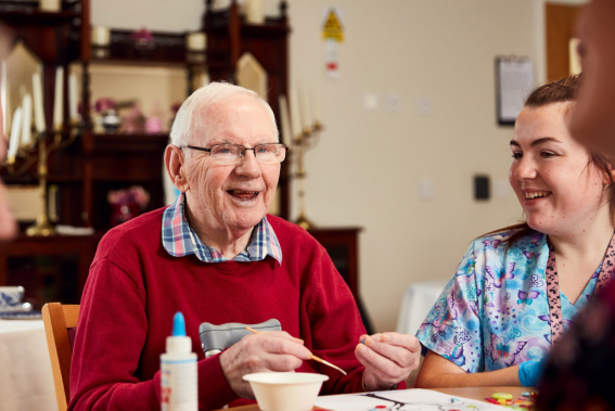 Man in red jumper laughing as he does artwork in Castlebridge Nursing Home